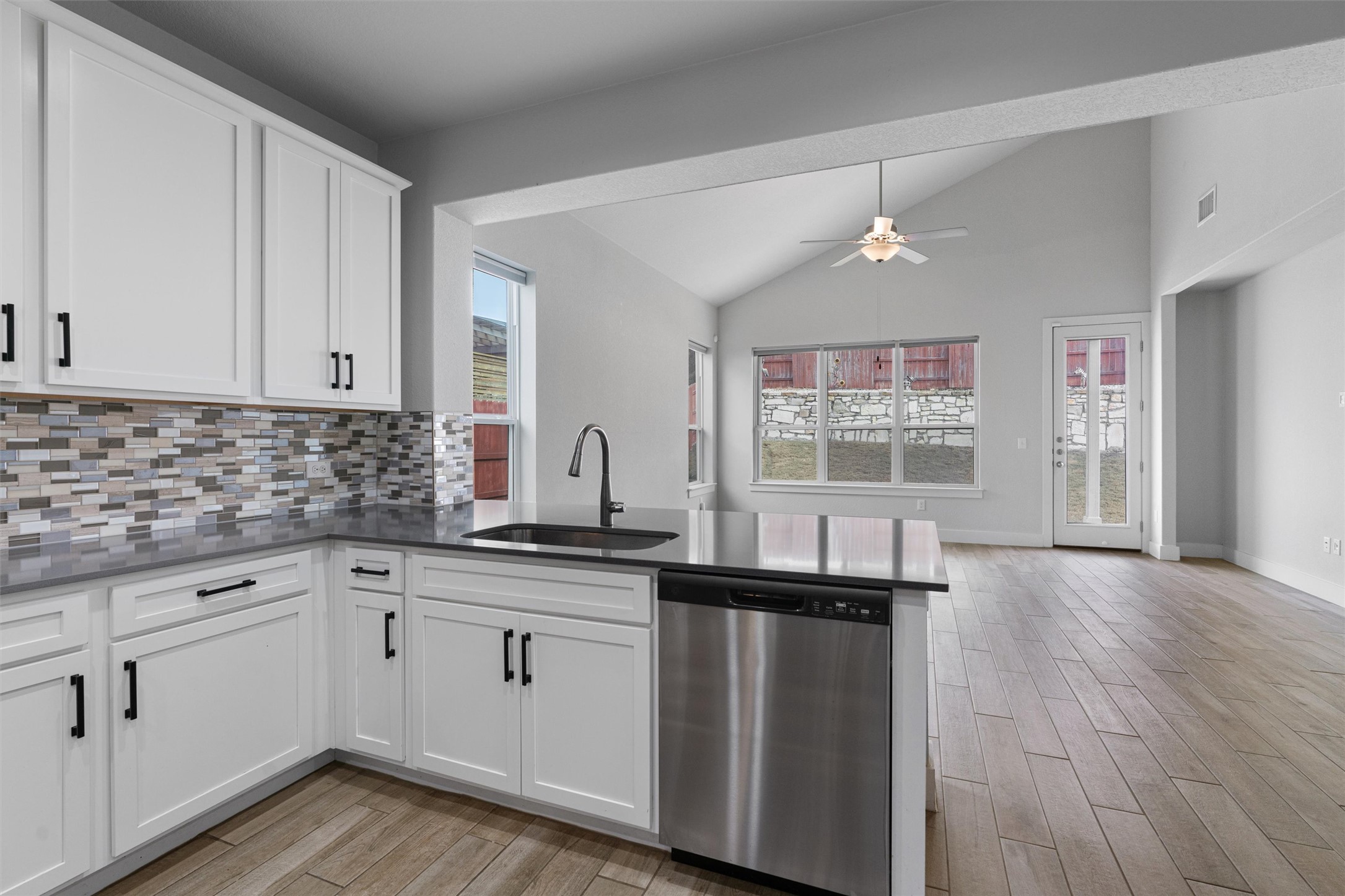 11217 Charger Way Manor, TX 78653 - Photo 34 of 35 Kitchen featuring stainless steel dishwasher, white cabinets, wood finish floors, open floor plan, and high vaulted ceiling