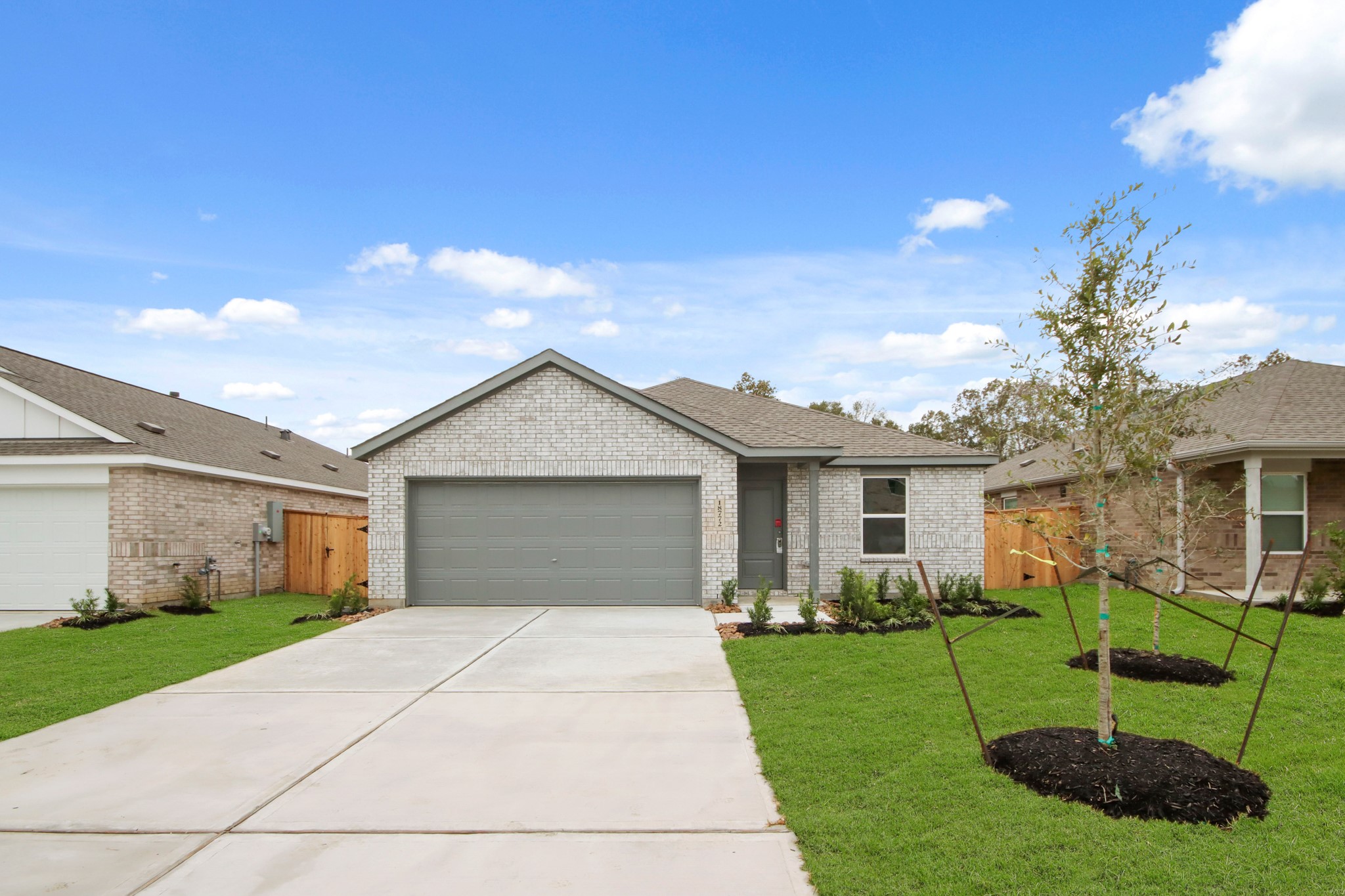 This charming single-story home features a modern brick exterior with a two-car garage. It has a neatly landscaped front yard with young trees and a spacious driveway, offering great curb appeal in a suburban neighborhood setting.