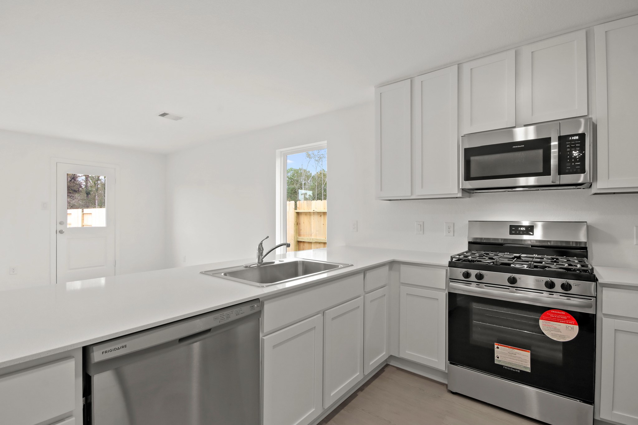 18779 Ribolla Drive New Caney, TX 77357 - Photo 9 of 24 Bright, modern kitchen with sleek white cabinetry and stainless steel appliances, including a gas stove and dishwasher. It features a spacious countertop with an integrated sink and ample natural light from the window and door.