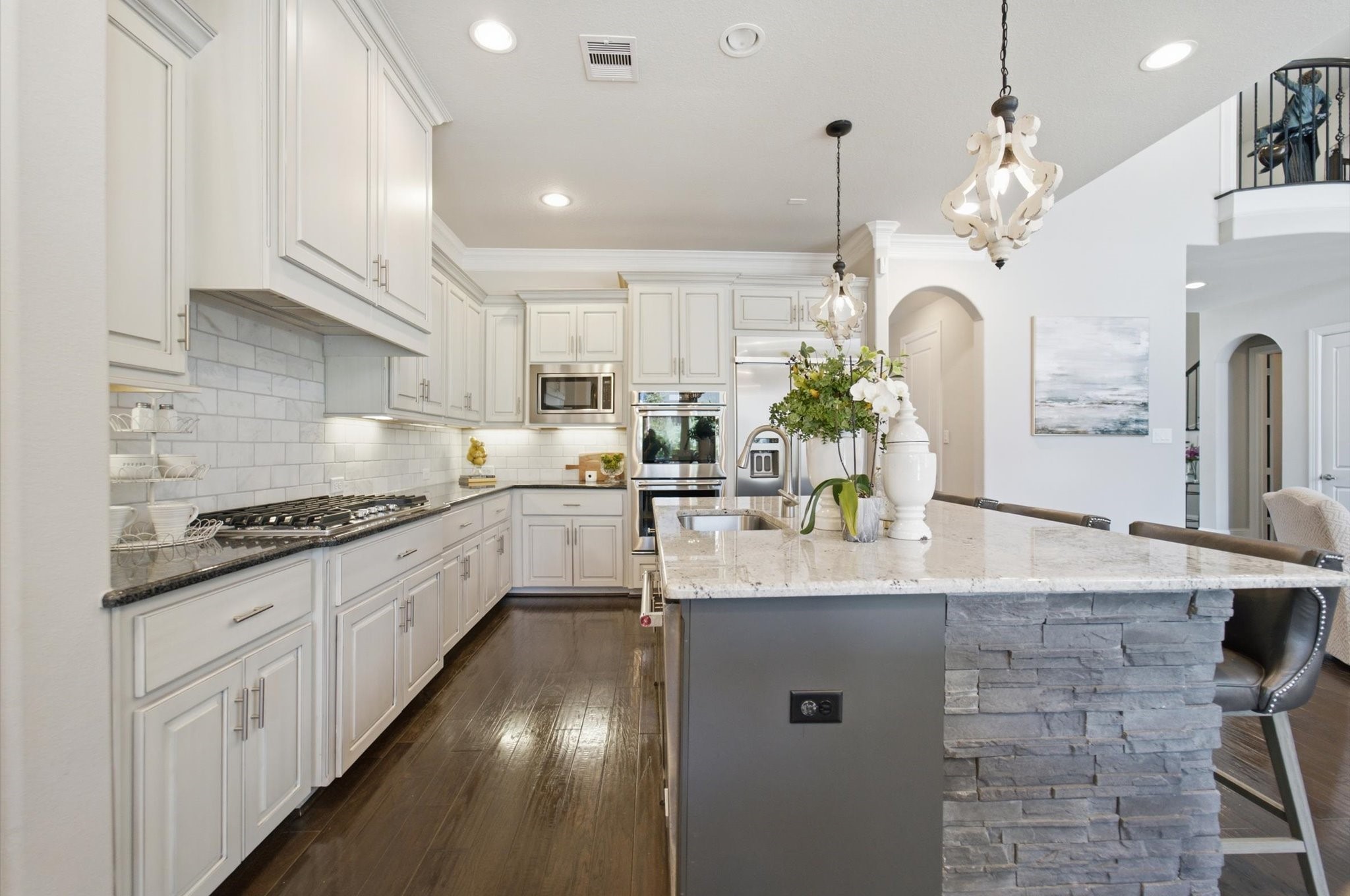23722 Thortons Park Lane Spring, TX 77389 - Photo 27 of 48 This spacious kitchen features elegant white cabinetry, a sleek granite island with stone accents, and modern stainless steel appliances. The dark hardwood floors complement the bright, airy ambiance, enhanced by stylish pendant lighting and a subway tile backsplash.