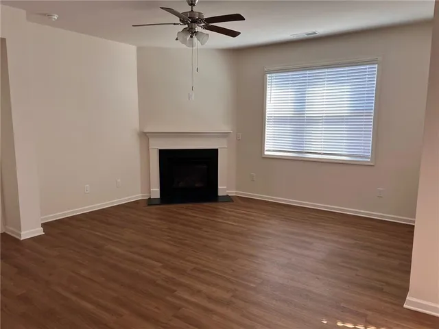 an empty room with wooden floor a ceiling fan a fireplace and windows