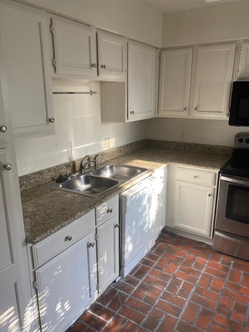 2110 Rio Grande Street, Unit 303 Austin, TX 78705 - Photo 3 of 7 A well-appointed kitchen showcasing white cabinetry, granite countertops, and durable brick flooring.