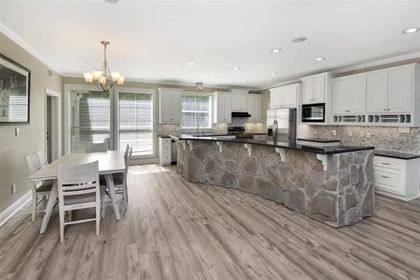 a kitchen with stainless steel appliances granite countertop a stove top oven a sink dishwasher a dining table and chairs with wooden floor