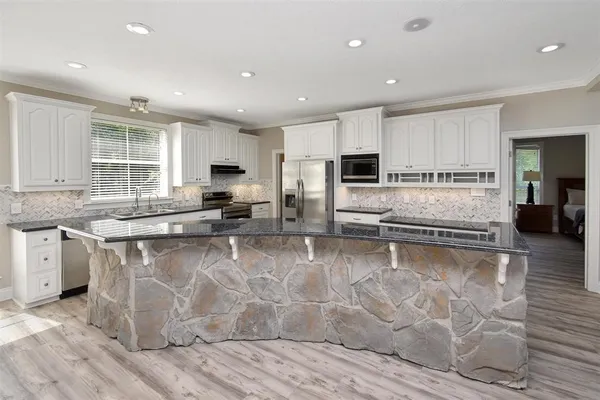 a large kitchen with granite countertop a large counter top stainless steel appliances and windows