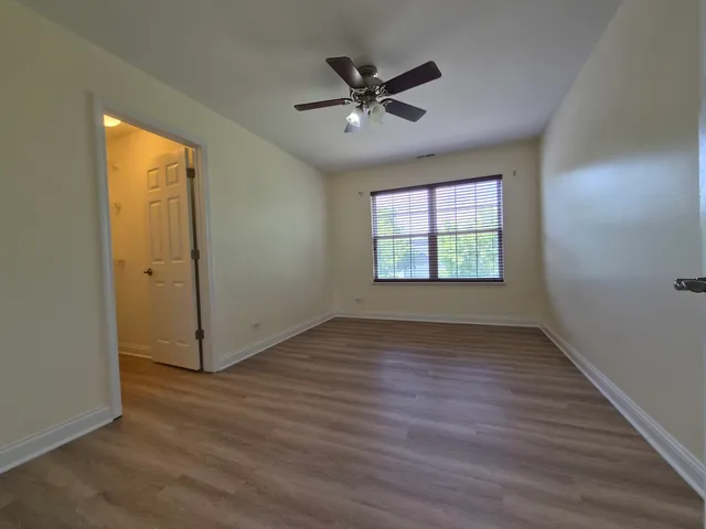 an empty room with wooden floor fan and windows