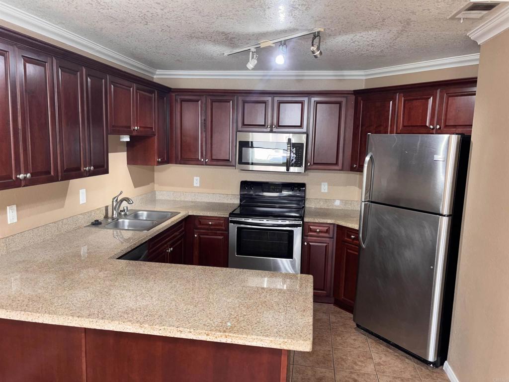 3545 Paseo De Francisco, Unit 225 Oceanside, CA 92056 - Photo 7 of 34 a kitchen with stainless steel appliances granite countertop a refrigerator a stove and a sink with wooden cabinets