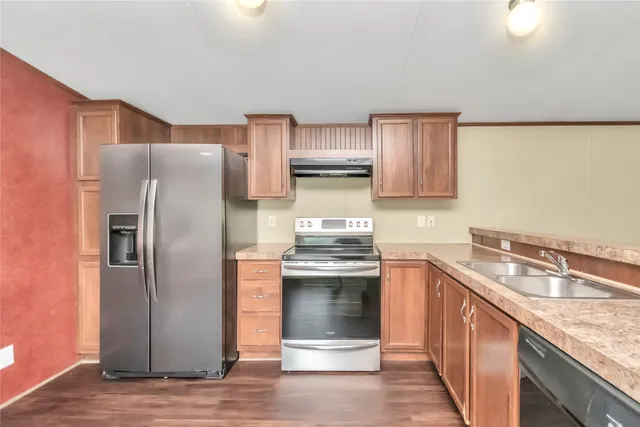a kitchen with stainless steel appliances granite countertop a refrigerator a stove and a sink with wooden cabinets