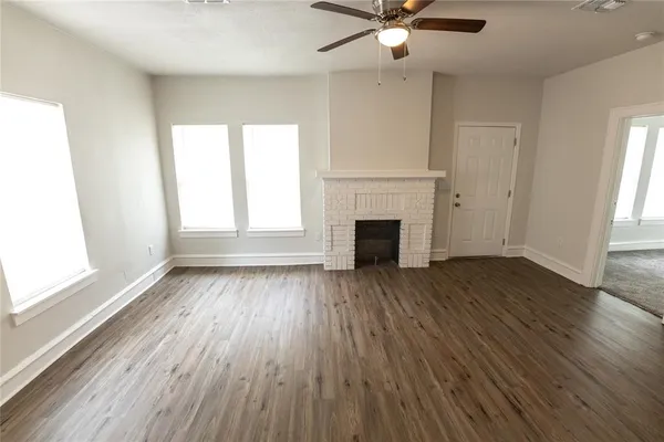 an empty room with wooden floor fireplace and windows