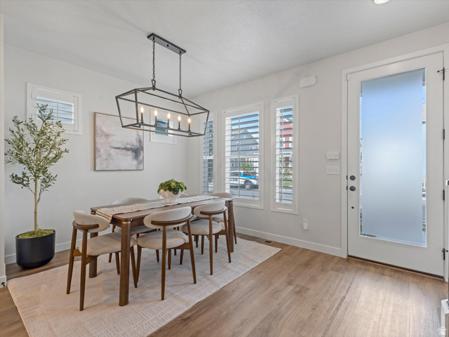 11759 South Watercourse Road South Jordan, UT 84009 - Photo 3 of 33 Dining area featuring wood-finish flooring, a contemporary linear chandelier, multiple windows with white louvered shutters, and a frosted glass-paneled exterior door