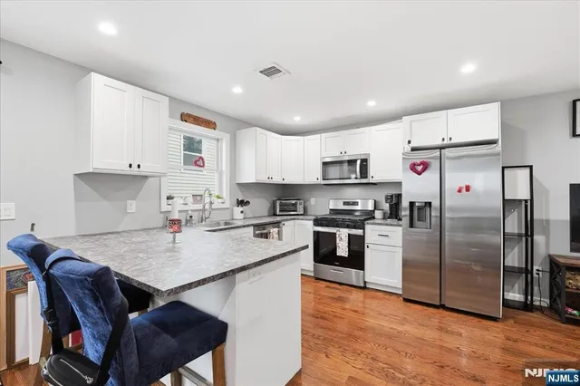 a kitchen with stainless steel appliances granite countertop a refrigerator a stove top oven a sink dishwasher and white cabinets with wooden floor