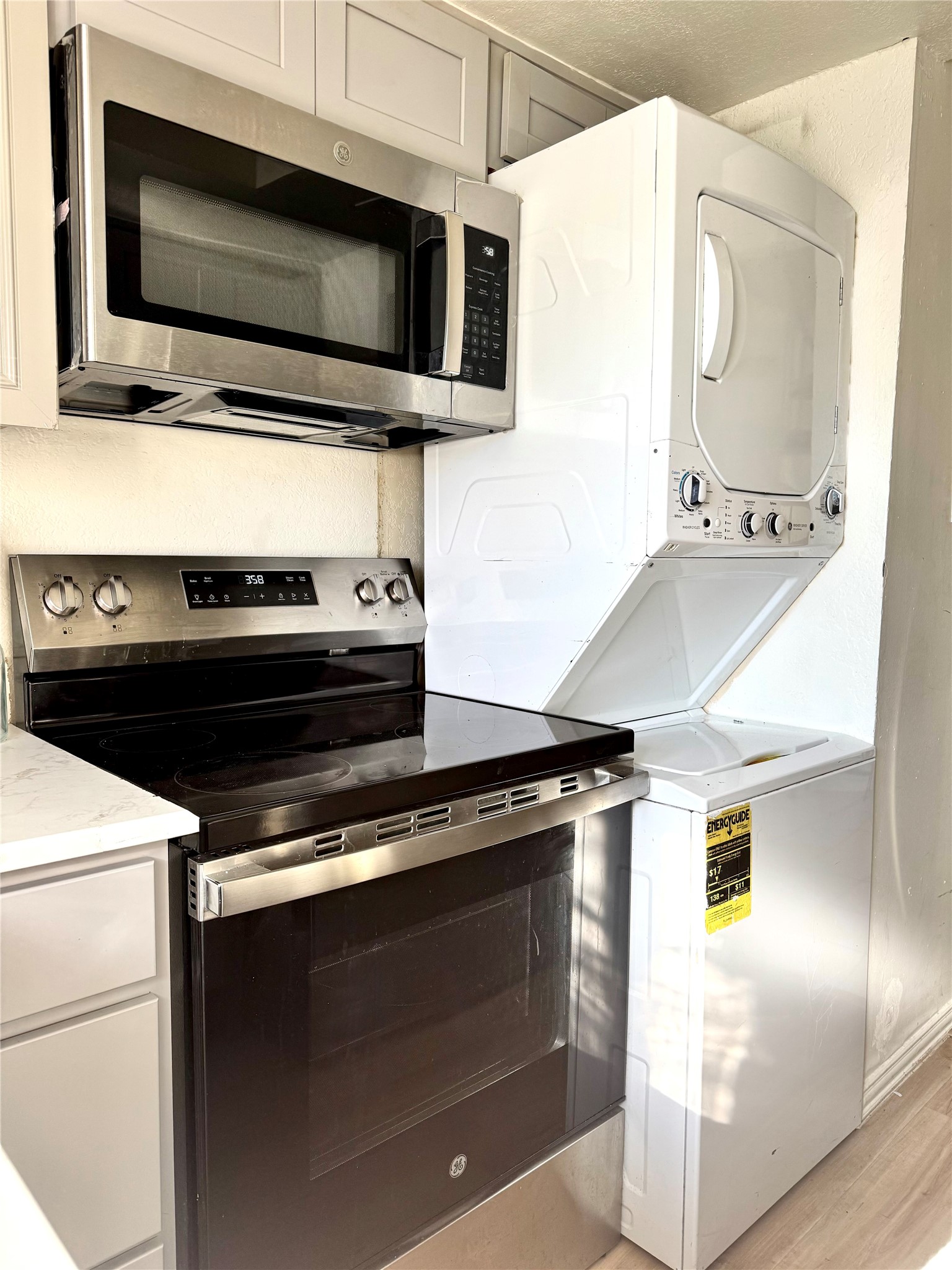 3506 Speedway, Unit 302 Austin, TX 78705 - Photo 9 of 27 Kitchen with stainless steel appliances, light wood-type flooring, stacked washer and clothes dryer, white cabinets, and light stone counters