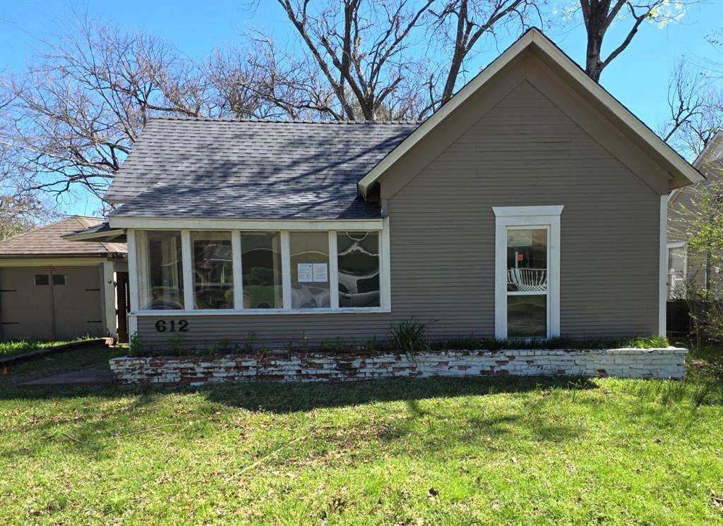 View of front facade featuring a sunroom, a front lawn, and a shingled roof