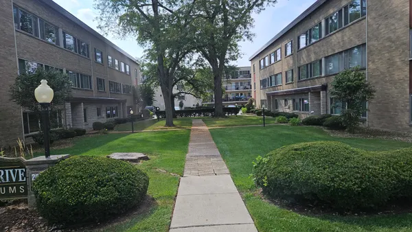 a view of a brick building next to a big yard and large trees