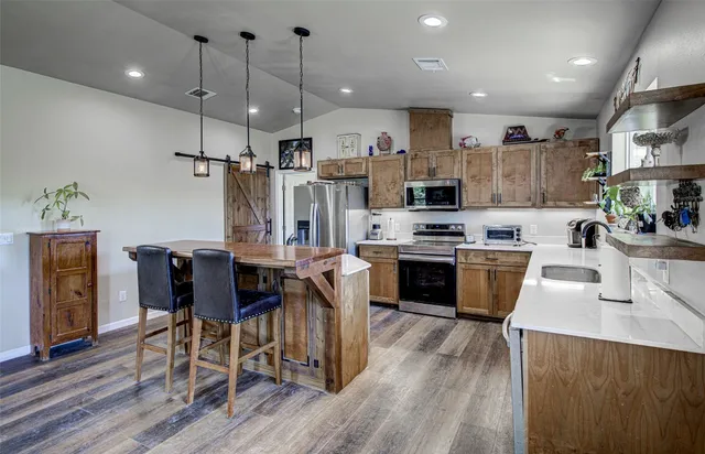 a kitchen with stainless steel appliances kitchen island granite countertop a table chairs and a refrigerator