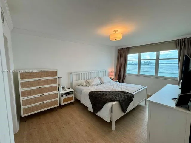 a spacious bedroom with a bed and a flat tv screen on dresser