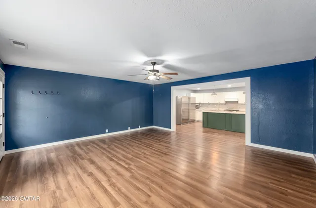 a view of an empty room with wooden floor and a kitchen