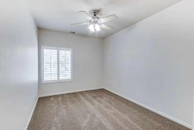 an empty room with chandelier fan and windows