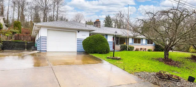 a view of a white house with a yard plants and large tree