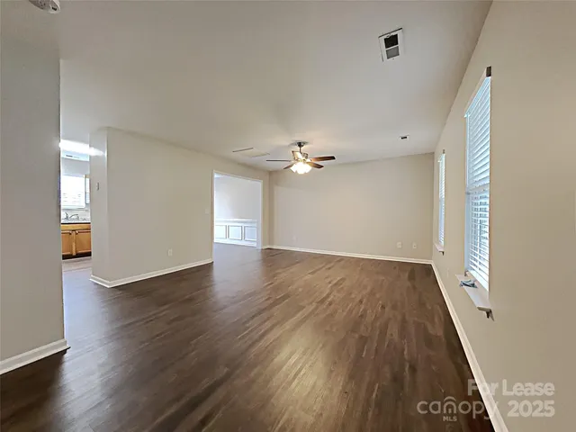 an empty room with wooden floor chandelier fan and windows