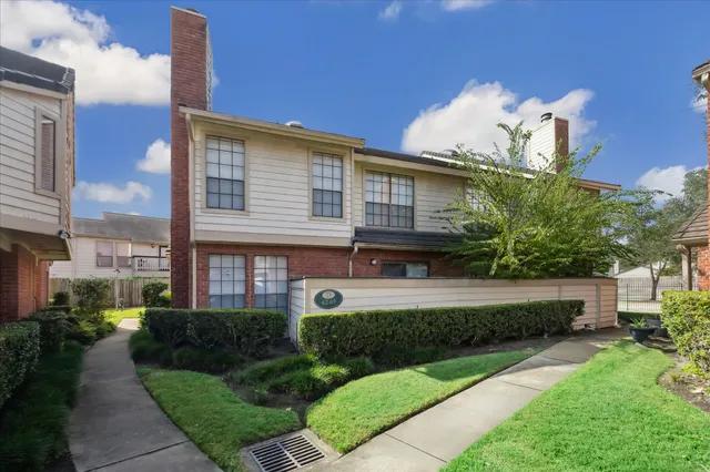 a view of a house with a yard plants and large tree