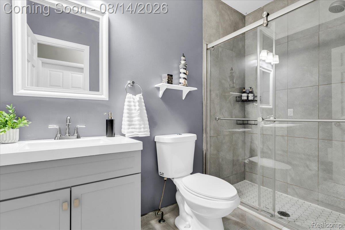 47321 Susan Road Macomb, MI 48044 - Photo 19 of 46 Vanity with white countertop, chrome faucet, framed mirror, and a glass-enclosed shower with tile surround and rain showerhead