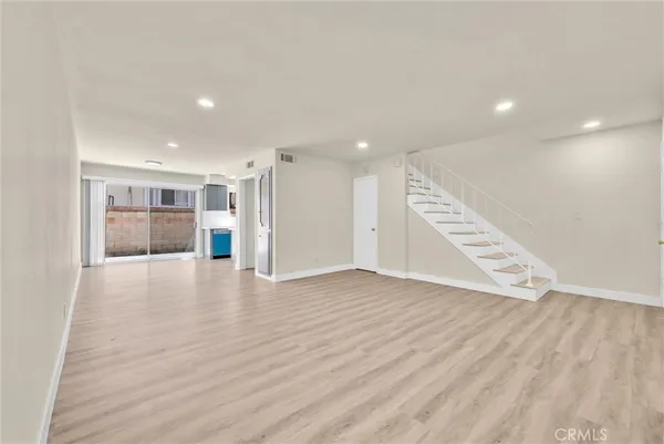 a view of an empty room with wooden floor and kitchen space