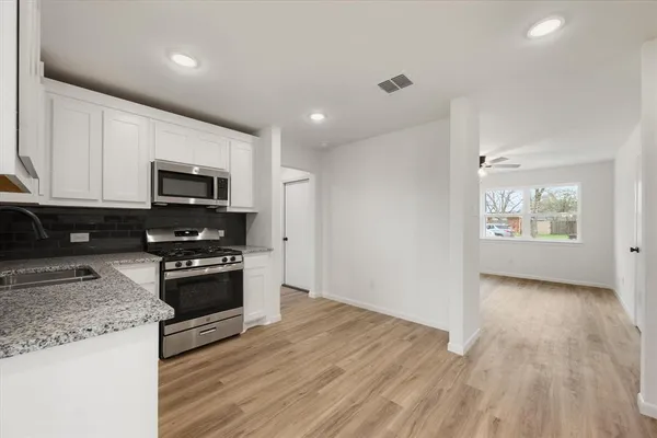 a kitchen with granite countertop a stove top oven a sink dishwasher a refrigerator and a microwave oven with wooden floor