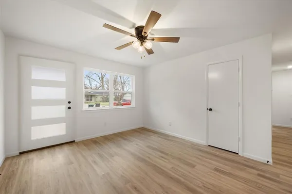 an empty room with wooden floor chandelier fan and windows
