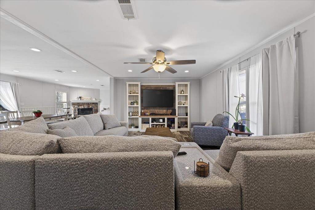 3605 Mockingbird Circle Cleburne, TX 76031 - Photo 11 of 40 Living room featuring ornamental molding, a stone fireplace, built in features, and ceiling fan