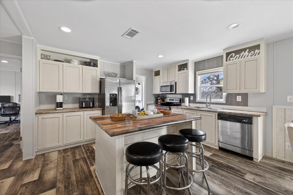 3605 Mockingbird Circle Cleburne, TX 76031 - Photo 13 of 40 Kitchen with estacked washer and dryer, stainless steel appliances, a breakfast bar, dark wood-style floors, and a center island