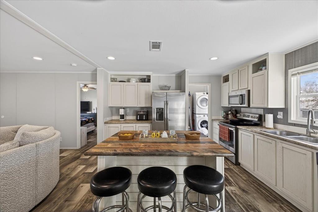 3605 Mockingbird Circle Cleburne, TX 76031 - Photo 14 of 40 Kitchen with appliances with stainless steel finishes, dark wood-style flooring, stacked washing machine and dryer, a kitchen bar, and dark stone counters