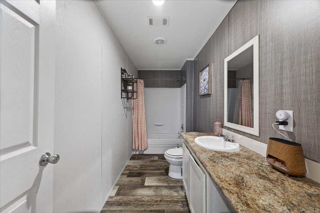 3605 Mockingbird Circle Cleburne, TX 76031 - Photo 33 of 40 Full bathroom featuring vanity, wallpapered walls, dark wood-style flooring, and shower / bath combo with shower curtain