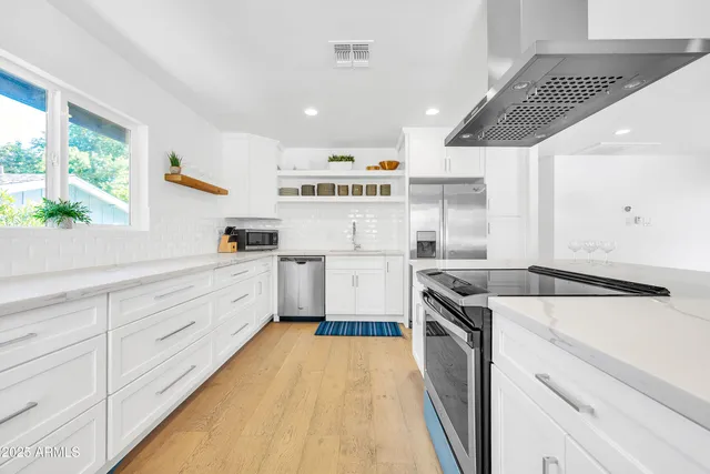 a kitchen with stainless steel appliances kitchen island granite countertop a dining table chairs and a refrigerator