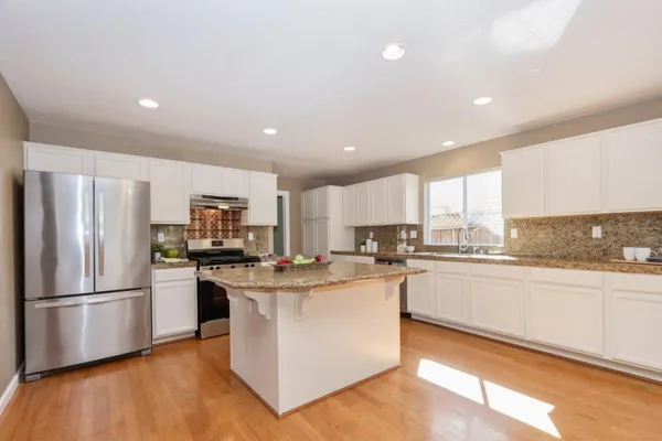 a kitchen with stainless steel appliances a refrigerator a stove top oven and white cabinets