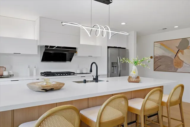 a kitchen with stainless steel appliances granite countertop a refrigerator a sink a stove a dining table and chairs with wooden floor