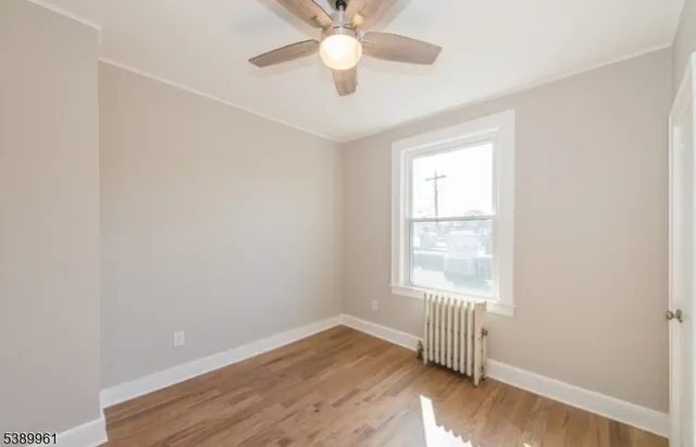 an empty room with wooden floor ceiling fan and windows