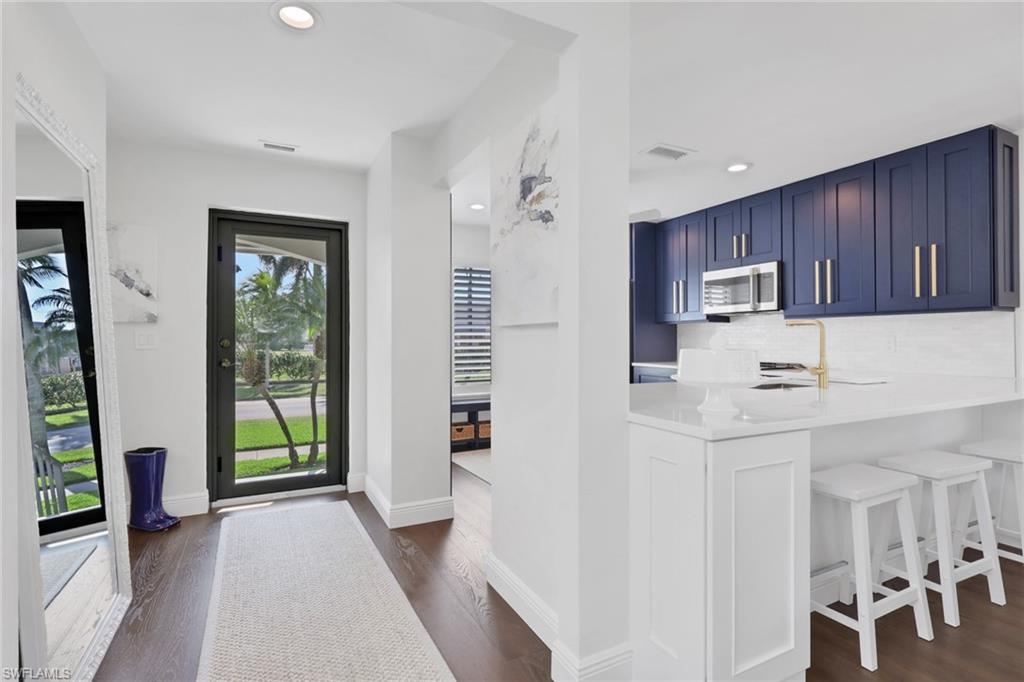 605 8th Avenue South, Unit 605 Naples, FL 34102 - Photo 3 of 50 Kitchen featuring blue cabinets, backsplash, a kitchen breakfast bar, light stone countertops, and stainless steel microwave