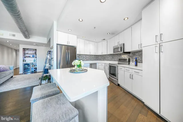 a kitchen with stainless steel appliances kitchen island granite countertop a refrigerator a stove a sink dishwasher and white cabinets with wooden floor
