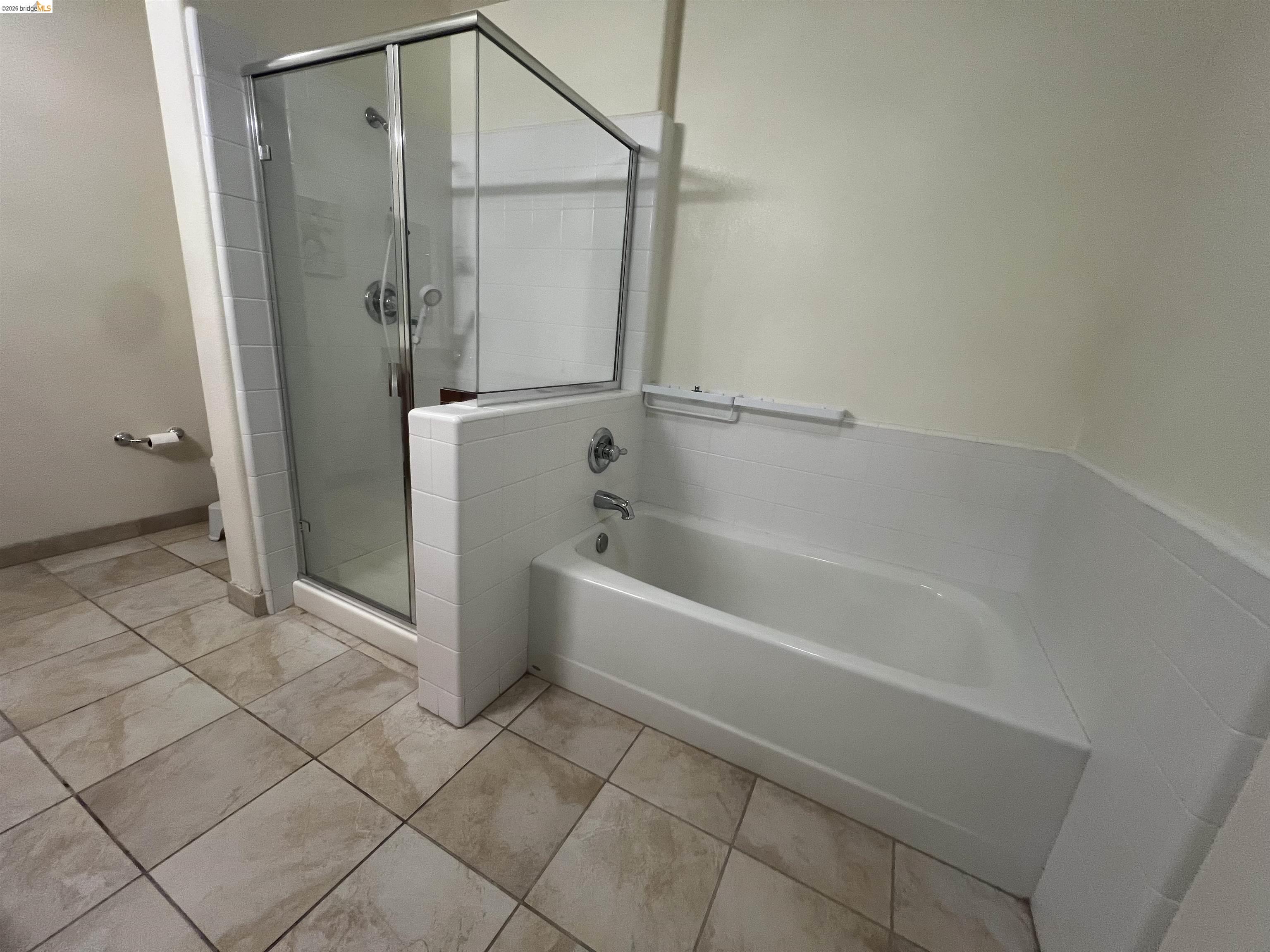 423 7th Street, Unit 313 Oakland, CA 94607 - Photo 10 of 11 Bathroom featuring a glass-enclosed shower, a built-in bathtub with white tile surround, and large format floor tiling