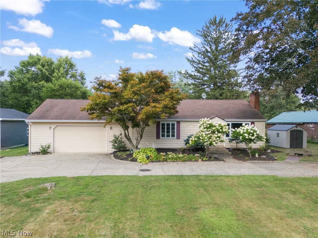 Single story home featuring a storage shed, a garage, driveway, a front yard, and a chimney