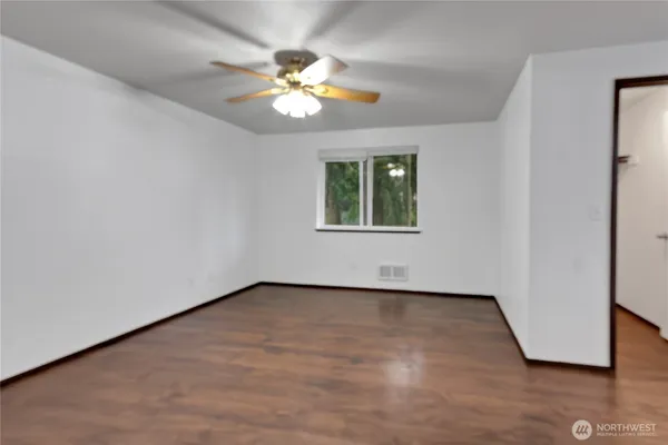 an empty room with wooden floor chandelier fan and windows