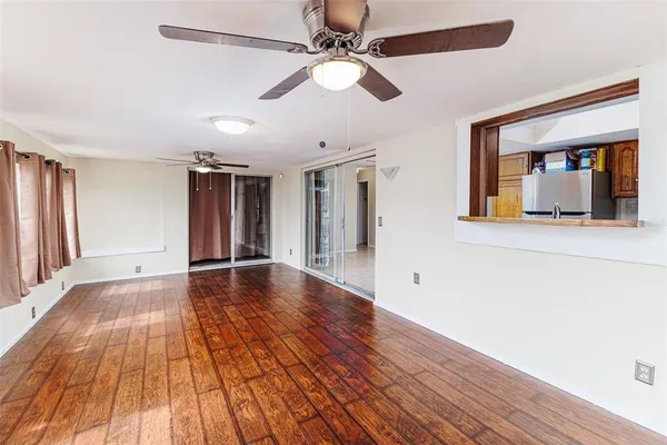 a view of an empty room with wooden floor and a ceiling fan