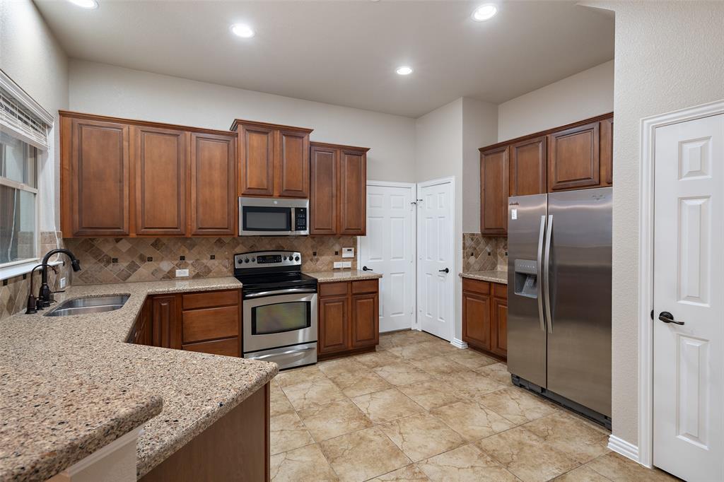 4245 Swan Forest Drive, Unit B Carrollton, TX 75010 - Photo 3 of 26 Kitchen with appliances with stainless steel finishes, backsplash, light stone countertops, recessed lighting, and brown cabinetry
