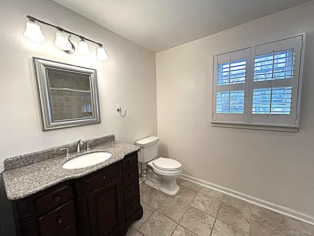 a bathroom with a granite countertop sink toilet a mirror and a window