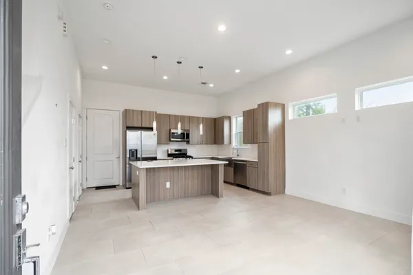 a large kitchen with a large counter top a sink a center island stainless steel appliances and a window