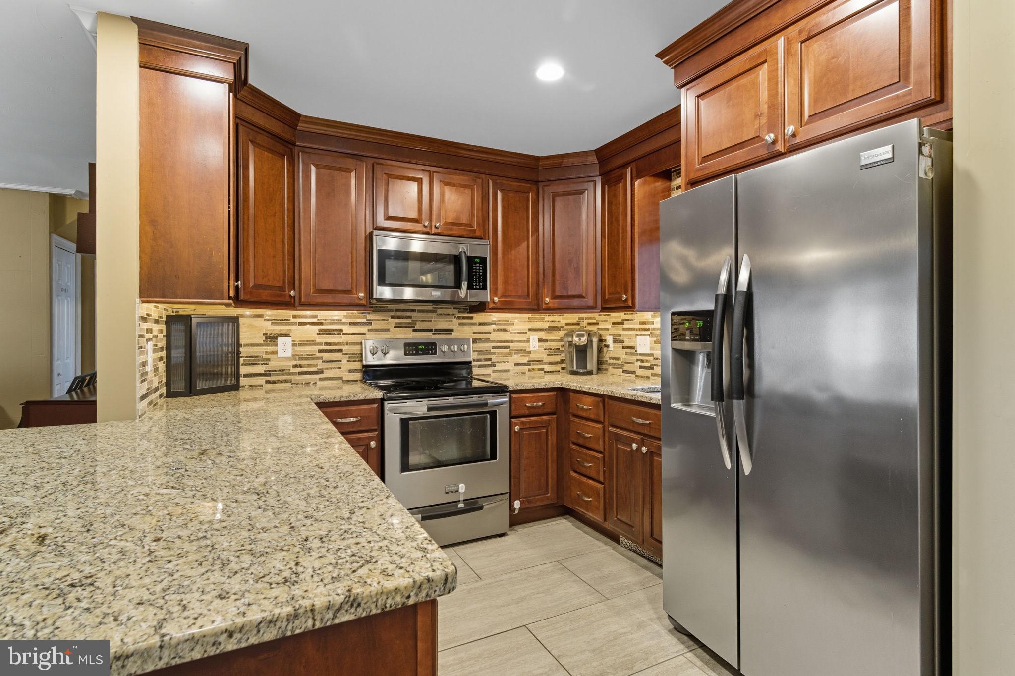 9 Newberry Lane Levittown, PA 19054 - Photo 4 of 36 a kitchen with stainless steel appliances granite countertop a refrigerator a stove and a sink with wooden cabinets