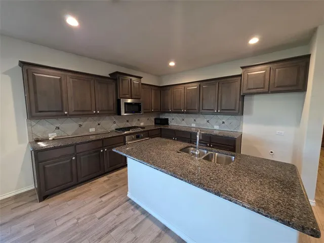 a kitchen with granite countertop wooden cabinets a stove a sink and dishwasher a refrigerator with wooden floor