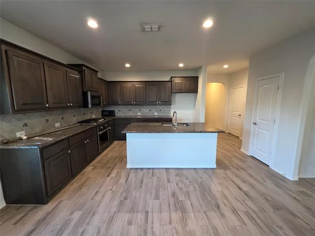 a large kitchen with stainless steel appliances granite countertop a stove a sink dishwasher and a oven with wooden cabinets