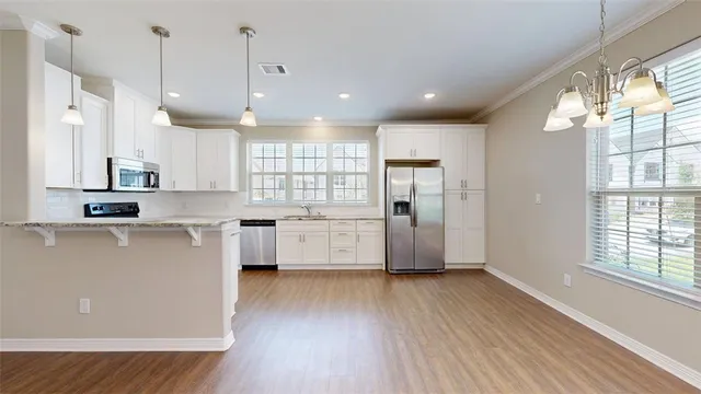 a kitchen with stainless steel appliances granite countertop a refrigerator a sink dishwasher a stove and white cabinets with wooden floor