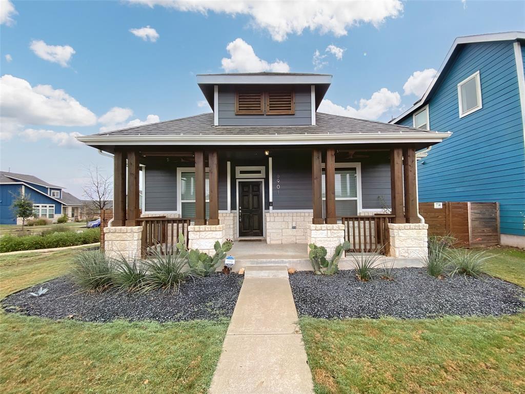 Contemporary exterior featuring gray siding, a covered porch with substantial wood columns and stone bases, a dark entry door, and dark gravel landscaping with desert plants